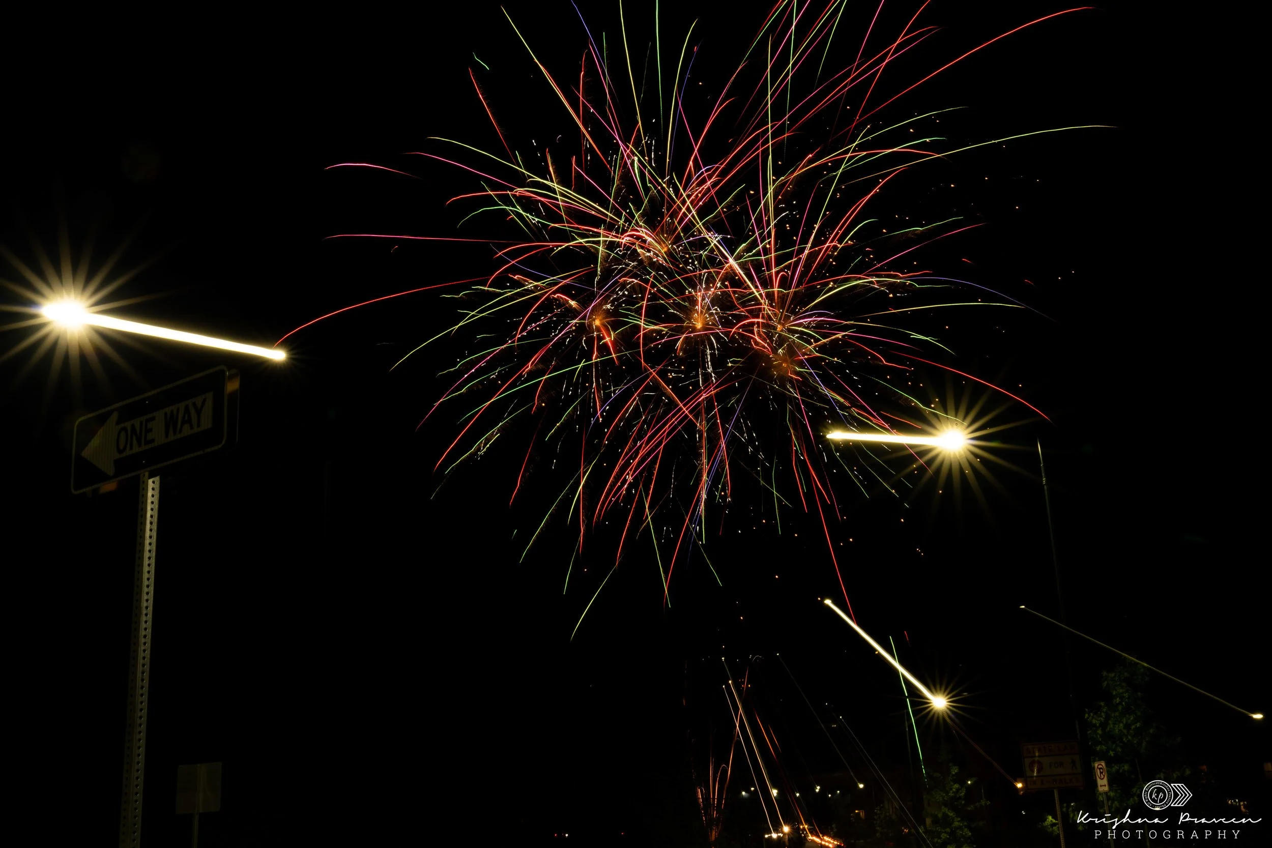 Colorful fireworks exploding in the night sky with streaks of red, green, yellow, and purple, illuminating the darkness.