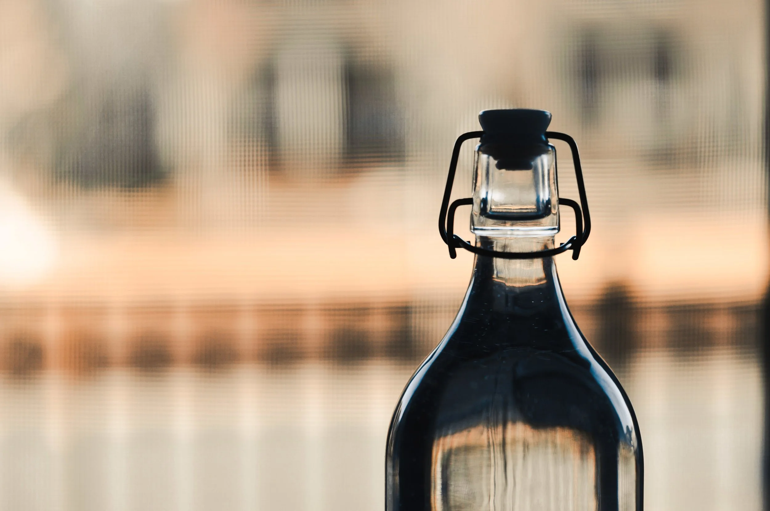 Close-up of a glass bottle with a swing-top closure, filled with a dark liquid, set against a blurred background.