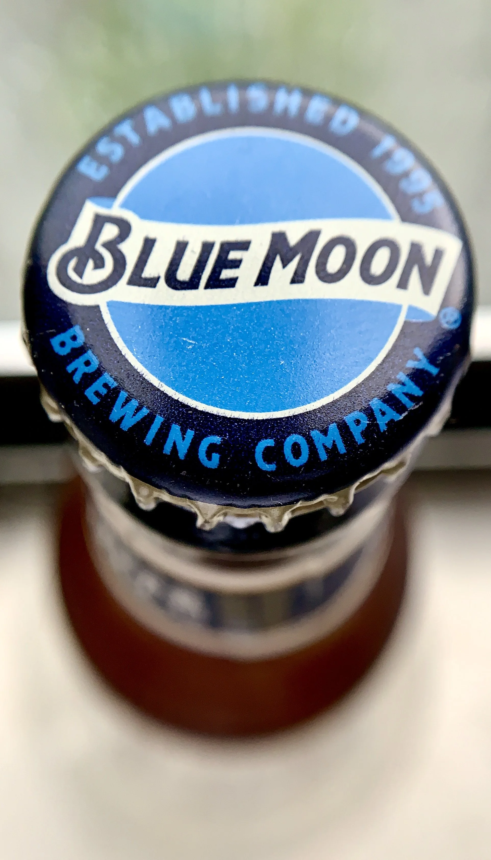 Close-up of the top of a bottle with a blue moon logo and a circular label reading 'Established 702, Brewing Company.'