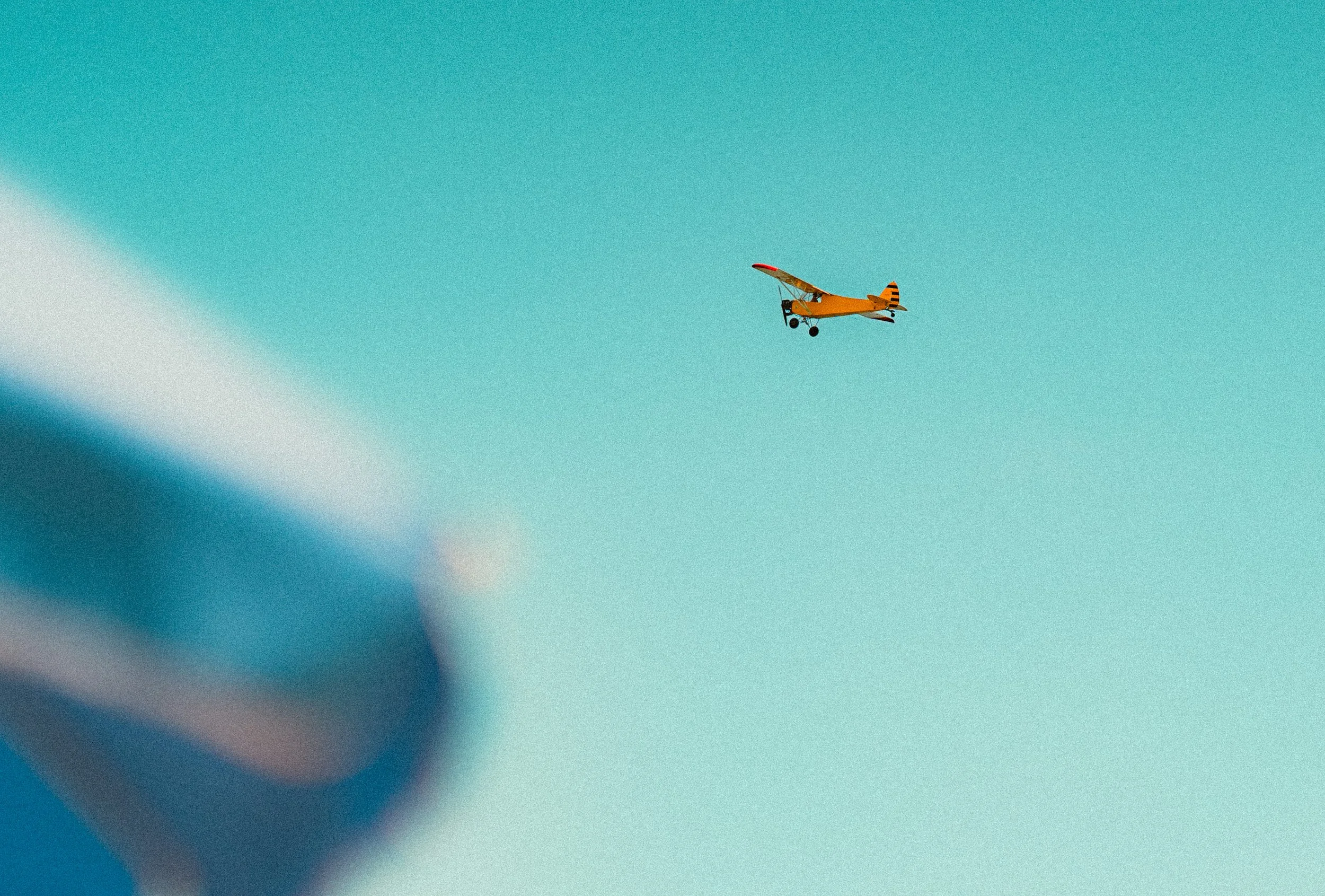 A small, bright yellow fixed-wing aircraft flying in a clear blue sky.