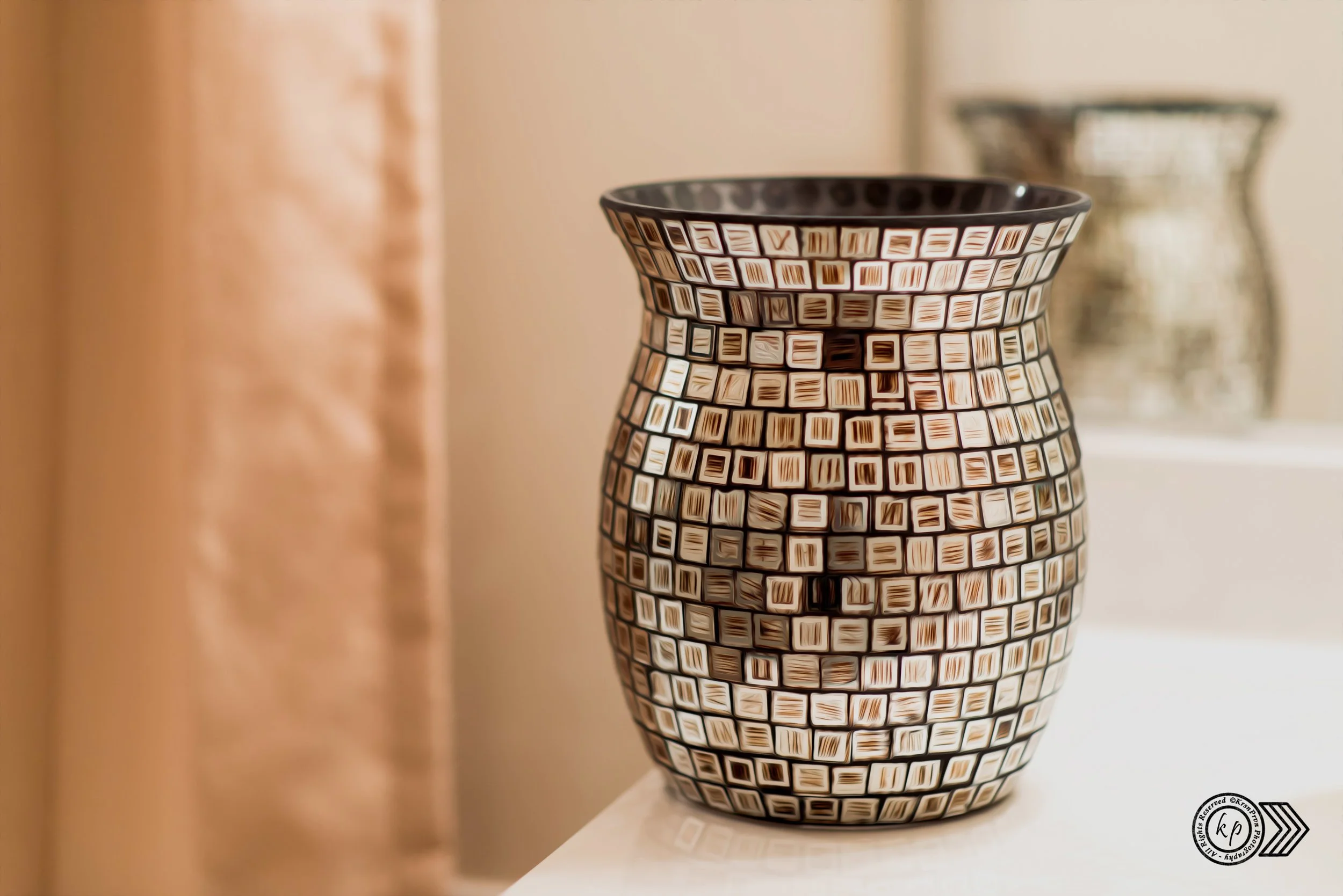Decorative ceramic vase with a geometric pattern of black and beige squares, placed on a white surface. Background is blurred with warm tones.