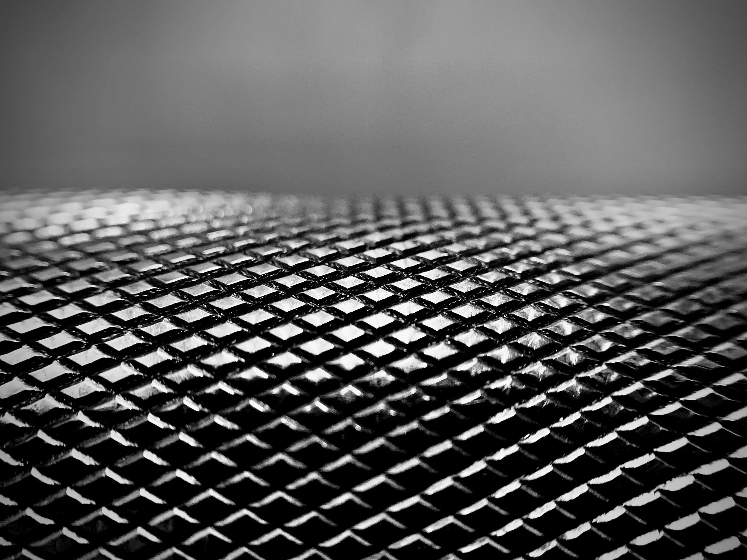 Close-up of a metallic textured surface, with a pattern of raised diamond shapes, in black and silver tones.