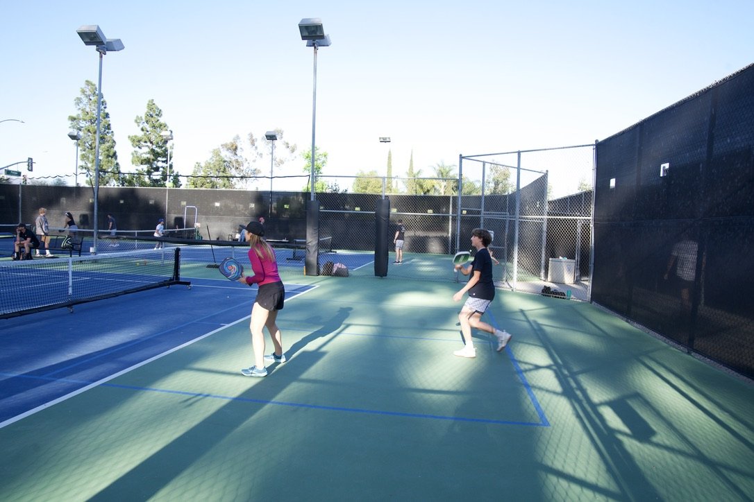 People playing pickleball on a court with net, fence, and outdoor lighting