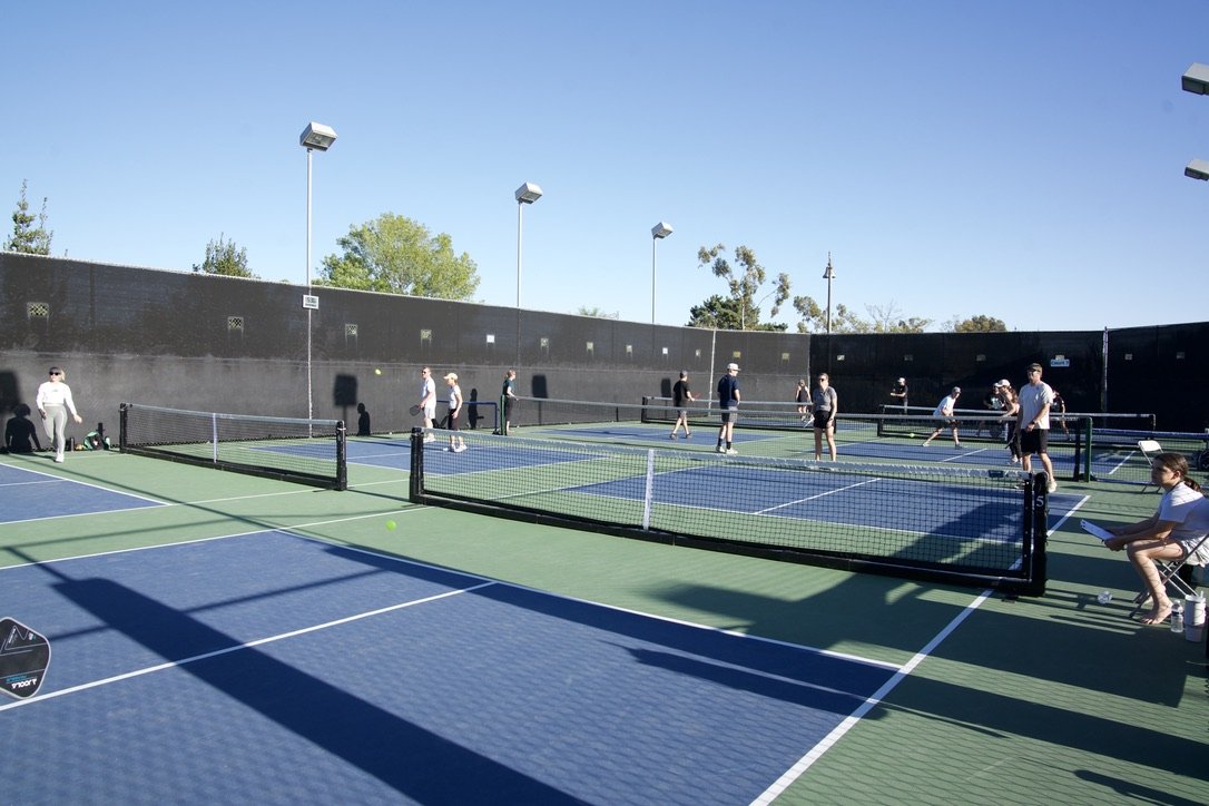 People playing pickleball on multiple courts outdoors on a sunny day.