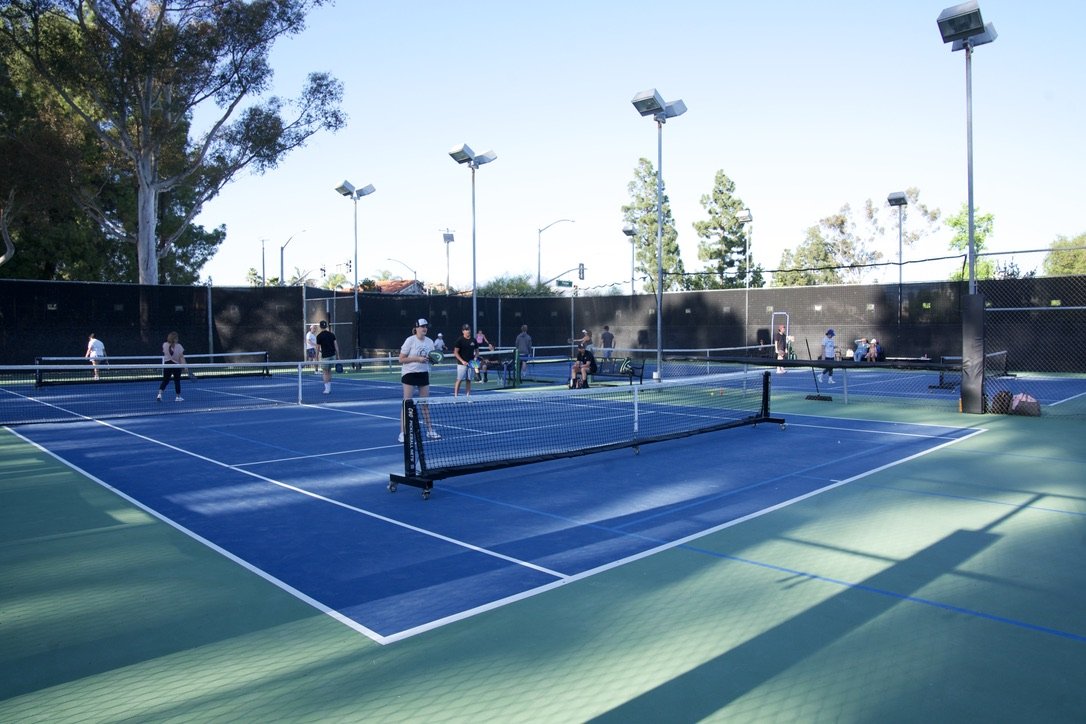 People playing tennis on multiple courts with trees and light poles in the background.