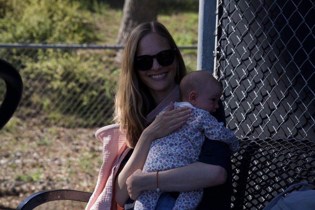 Woman with sunglasses smiling and holding a baby girl on a park bench