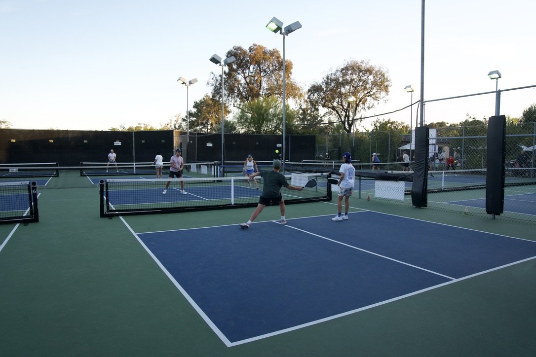 People playing pickleball on outdoor courts during the daytime.