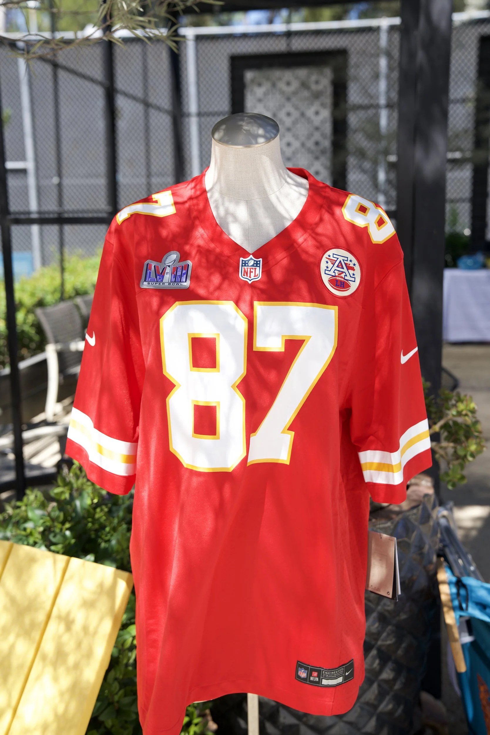 Red Kansas City Chiefs football jersey with number 87 displayed outdoors, decorated with Super Bowl LIV patch and other NFL patches.