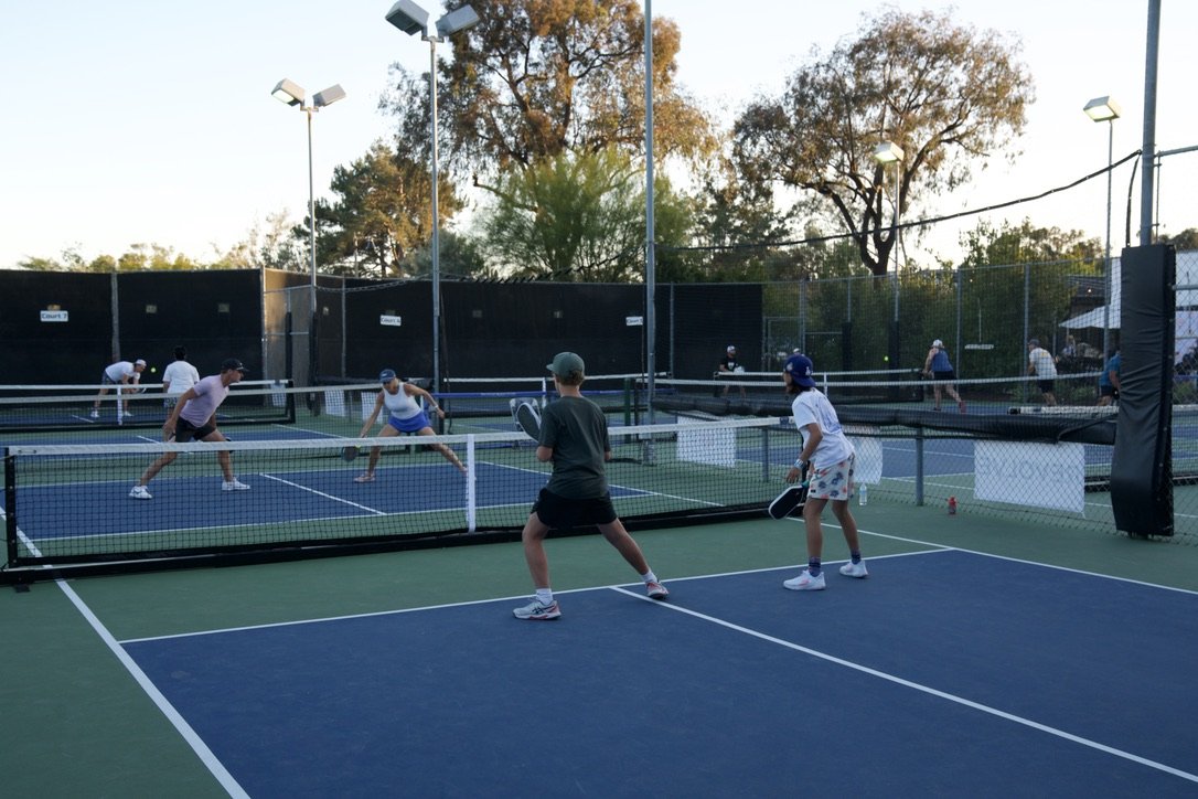 People playing pickleball on an outdoor court during the daytime.