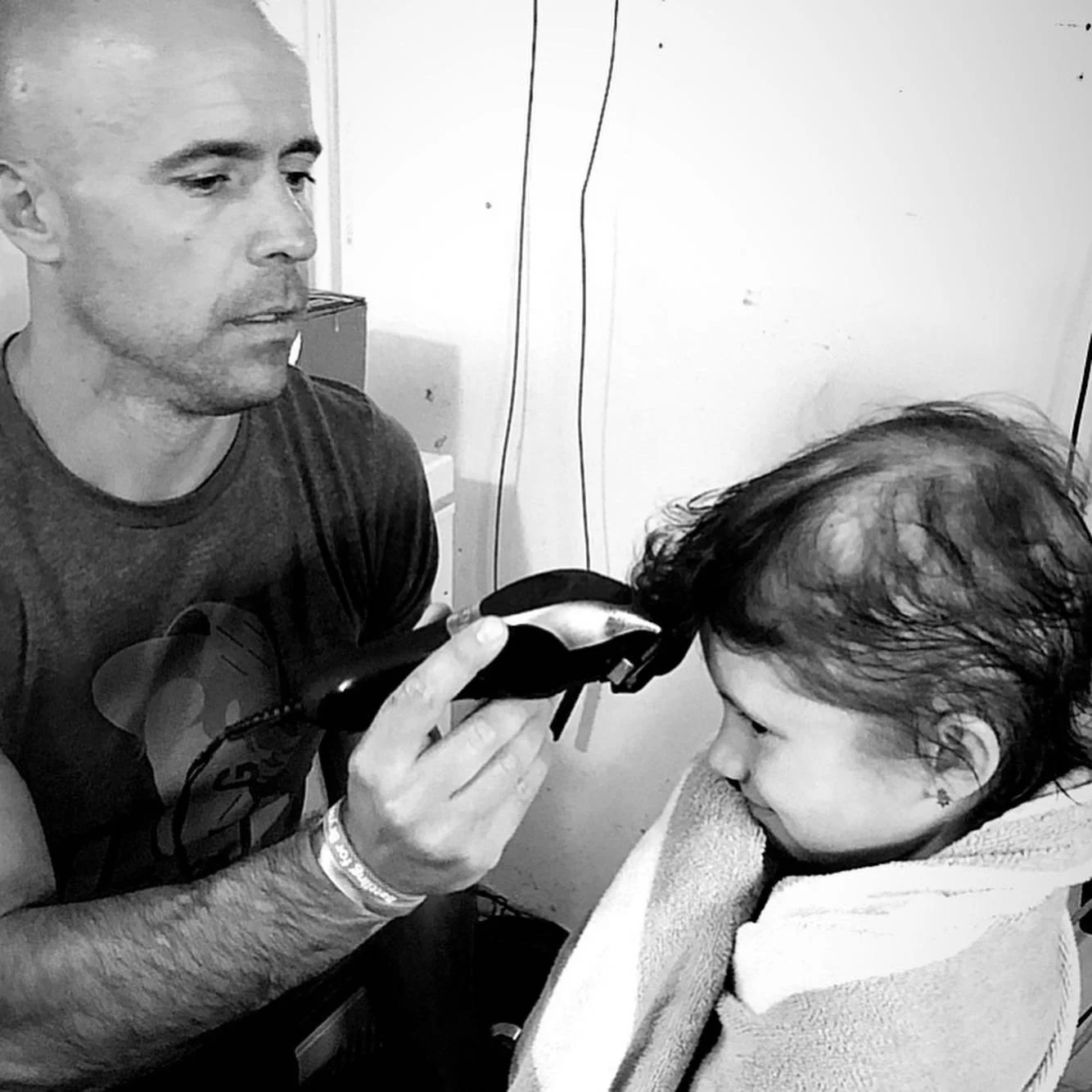 Man using hair clippers on a child wrapped in a towel, black and white image.