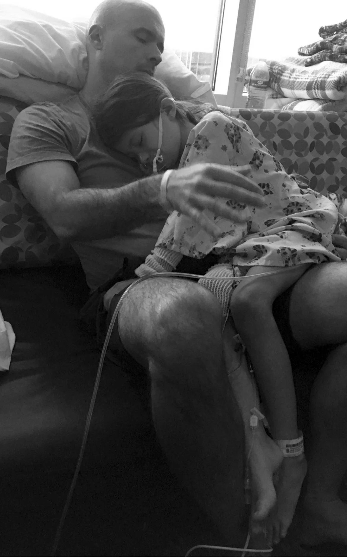 A man holding a child with medical tubes in a hospital setting.
