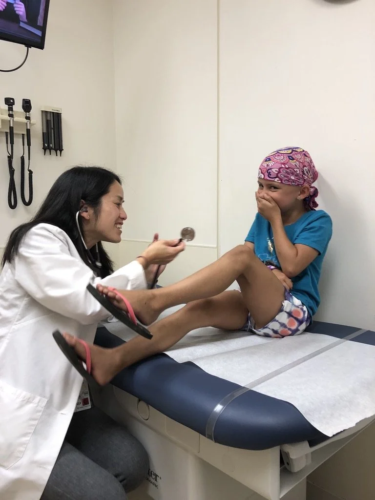 Doctor examining a smiling child wearing a bandana in a medical exam room.