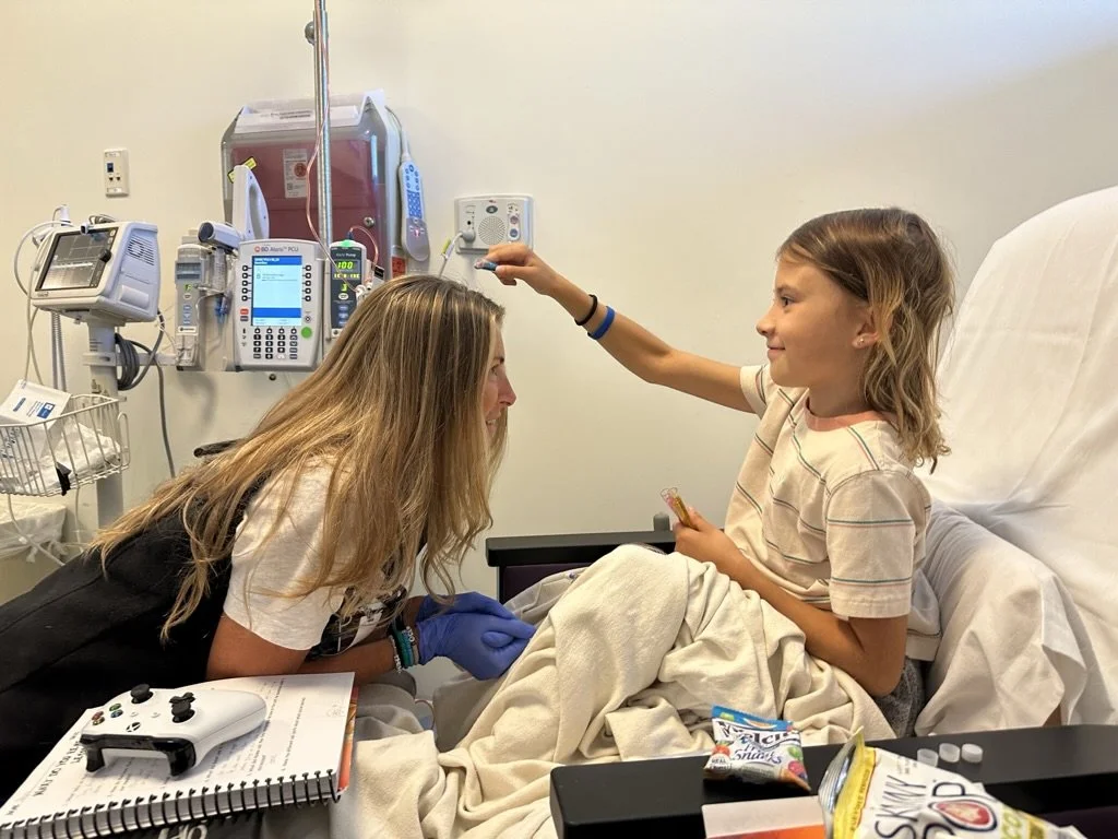 A child in a hospital bed interacting with a caregiver, surrounded by medical equipment and snacks.