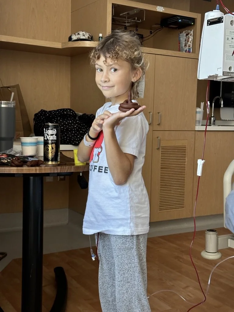 Child in a hospital room holding a molded clay figure; an IV bag is visible in the background.
