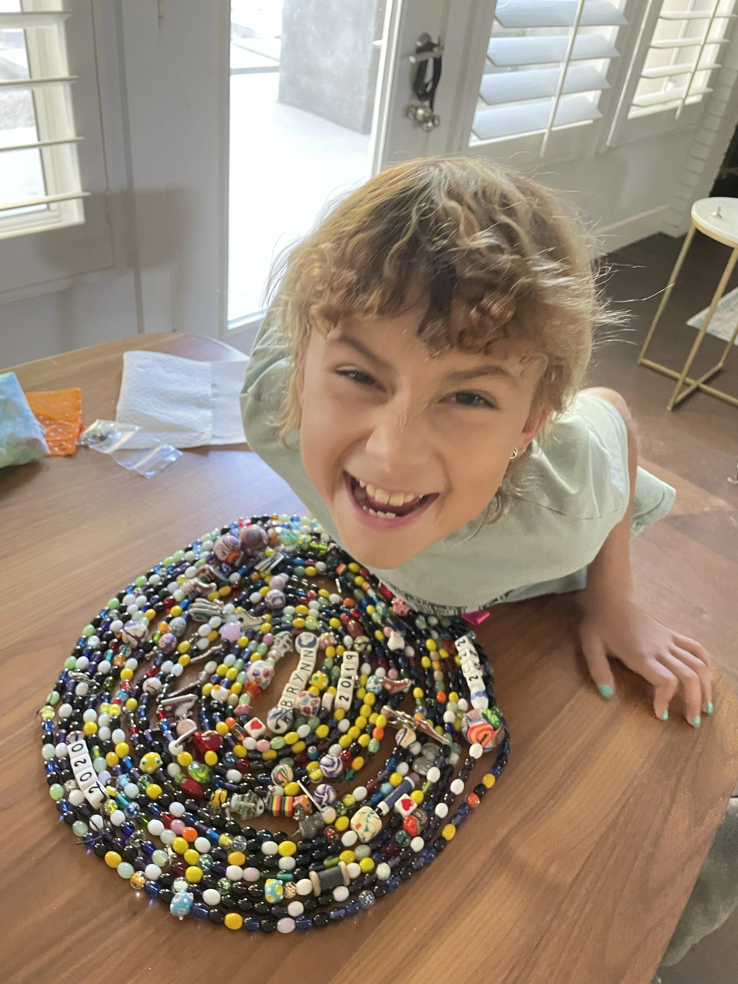 Child smiling next to a colorful bead necklace on a table.