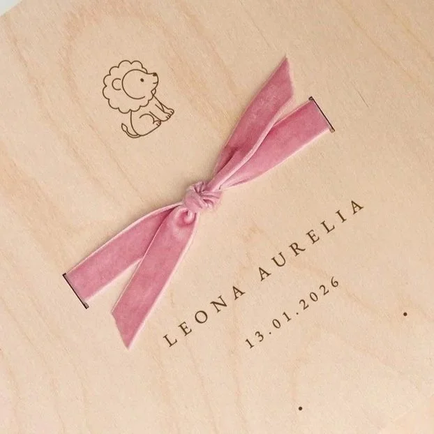 Eine Geschenkverpackung mit rosa Schleife, einem niedlichen Lauffröschen-Design und dem Namen 'Leona Aurelia' sowie dem Datum 13.01.2026.