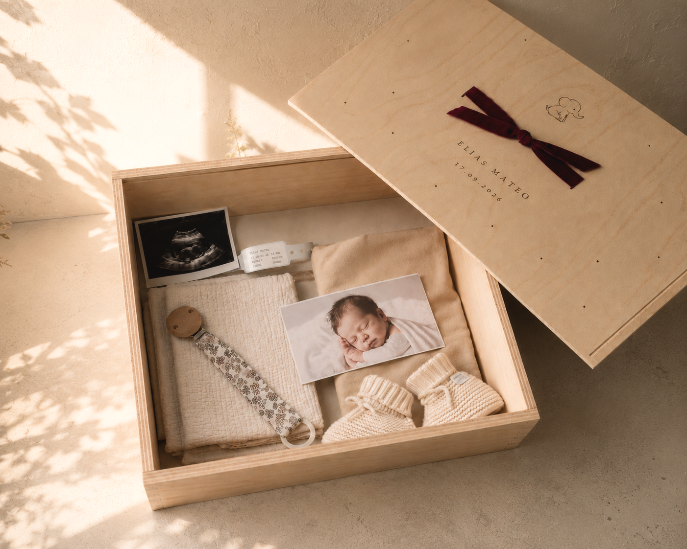Ein Schnupf, ein Ultraschallbild, ein kleines Babyfoto, Babyschuhe, ein Stoffbänder, eine Geburtsurkunde in einem Holzkasten, dazu eine Schachtel mit dem Namen Elias Mateo und Geburtsdatum.