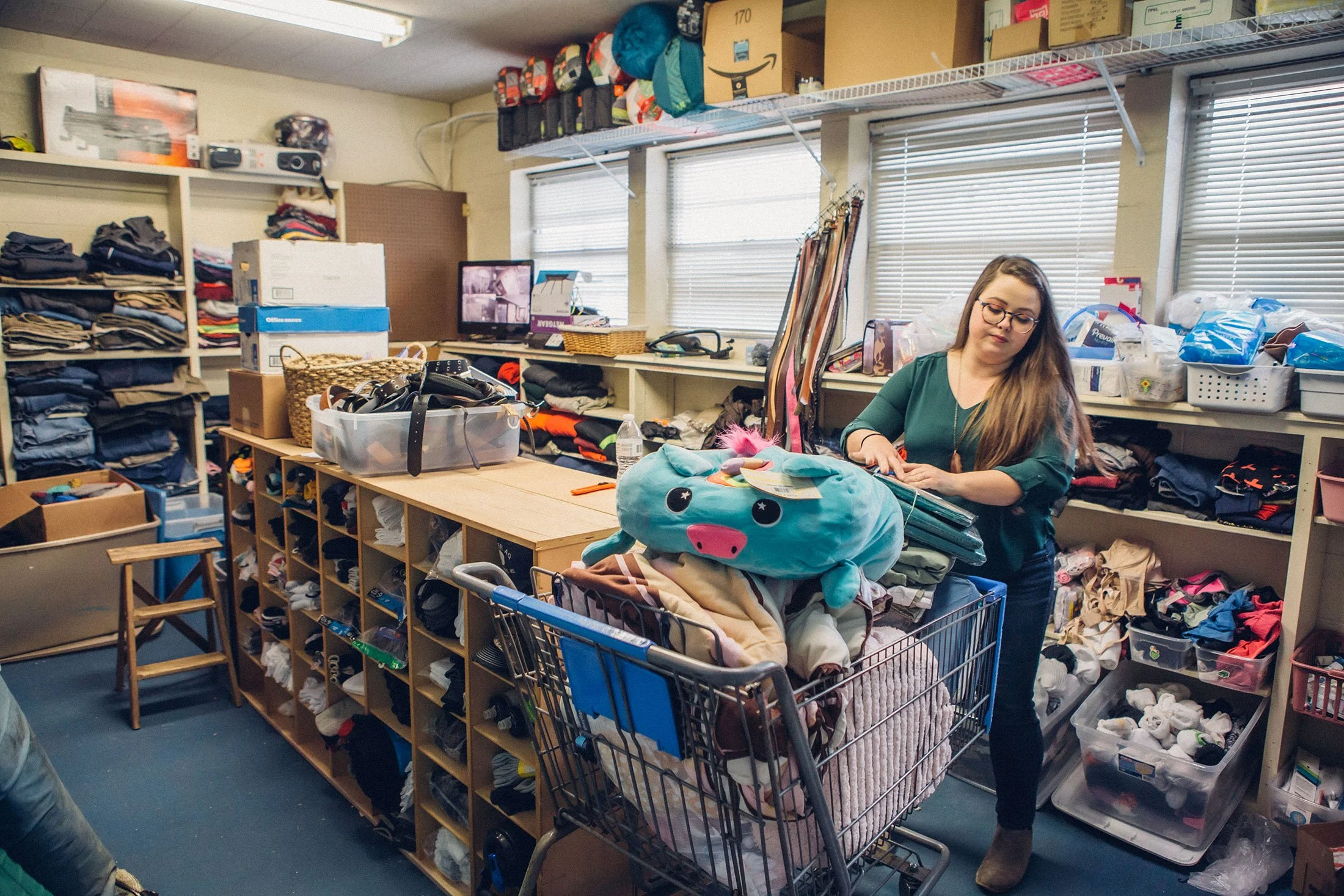 young woman pushes shopping cart in clothing room full of clothing