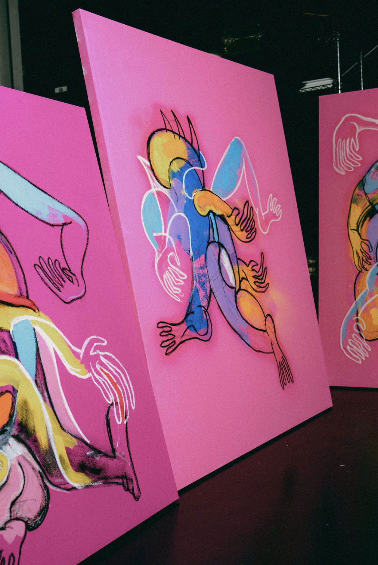 Large pink Caskey paintings featuring bold outlined figures, black linework and layers of vibrant color.