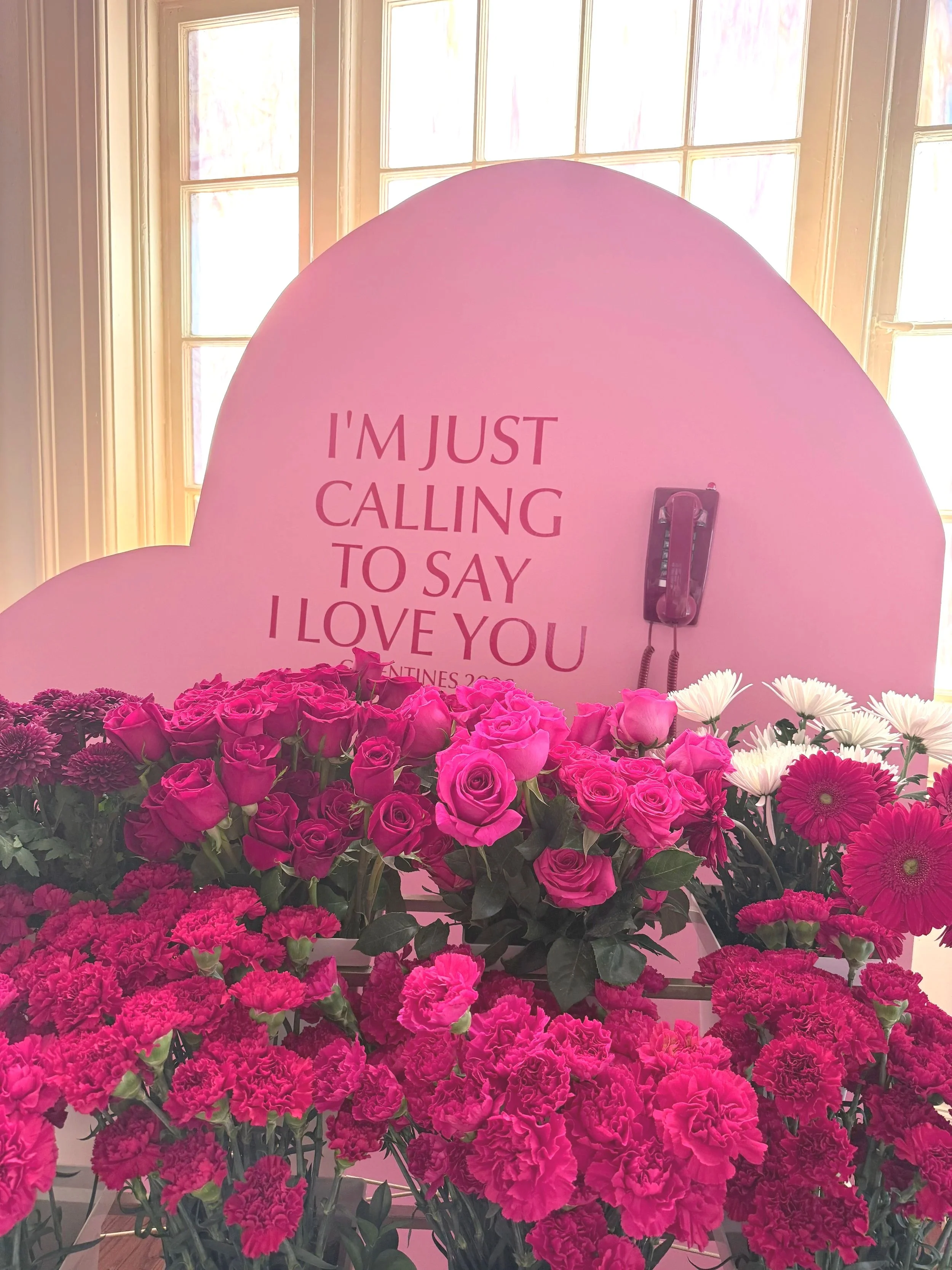 Pink heart sign reading “I’m just calling to say I love you” surrounded by pink and white flowers.