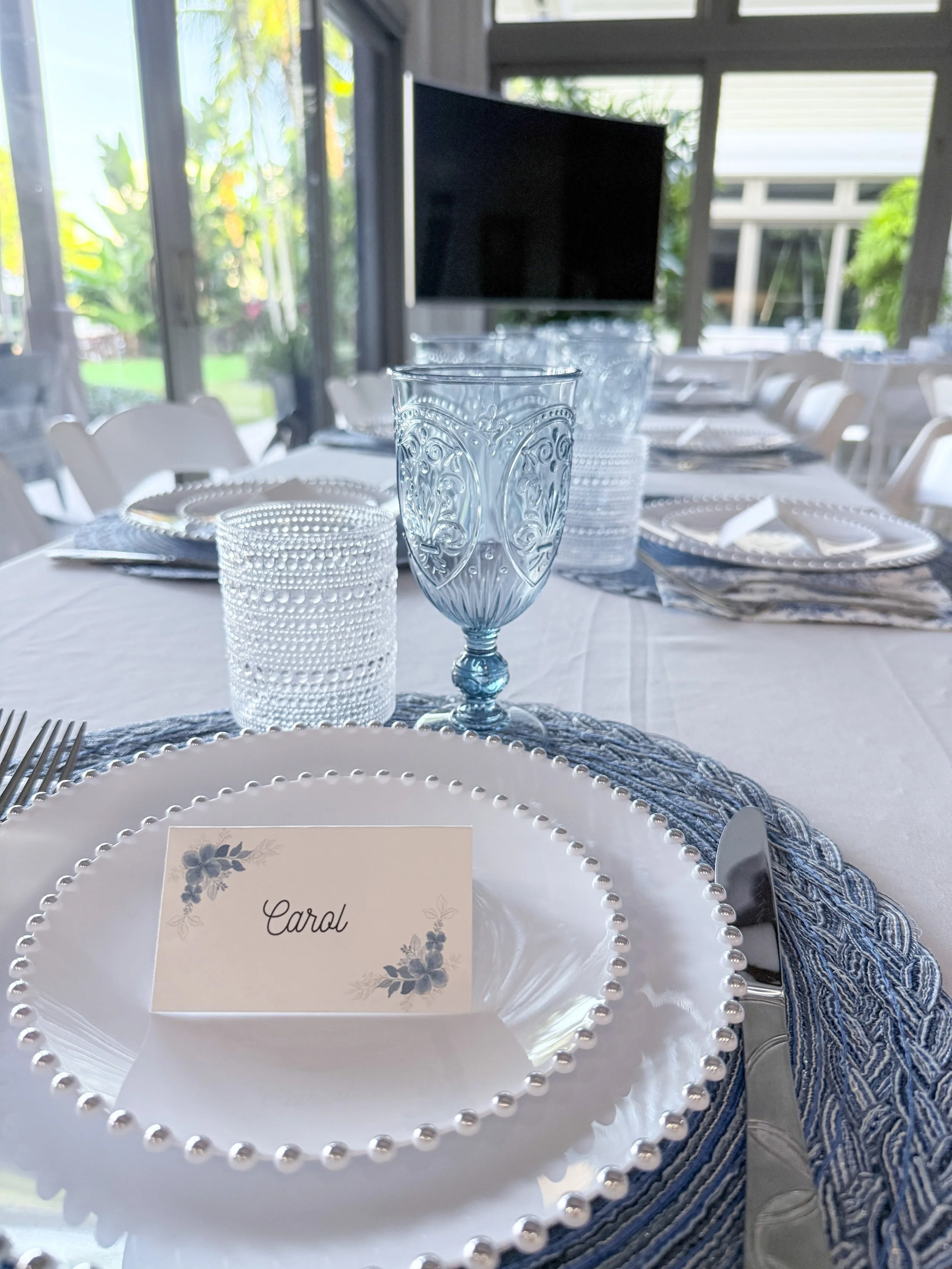 Formal tablescape with blue glassware, pearl-edged plates and a personalized place card for Carol.