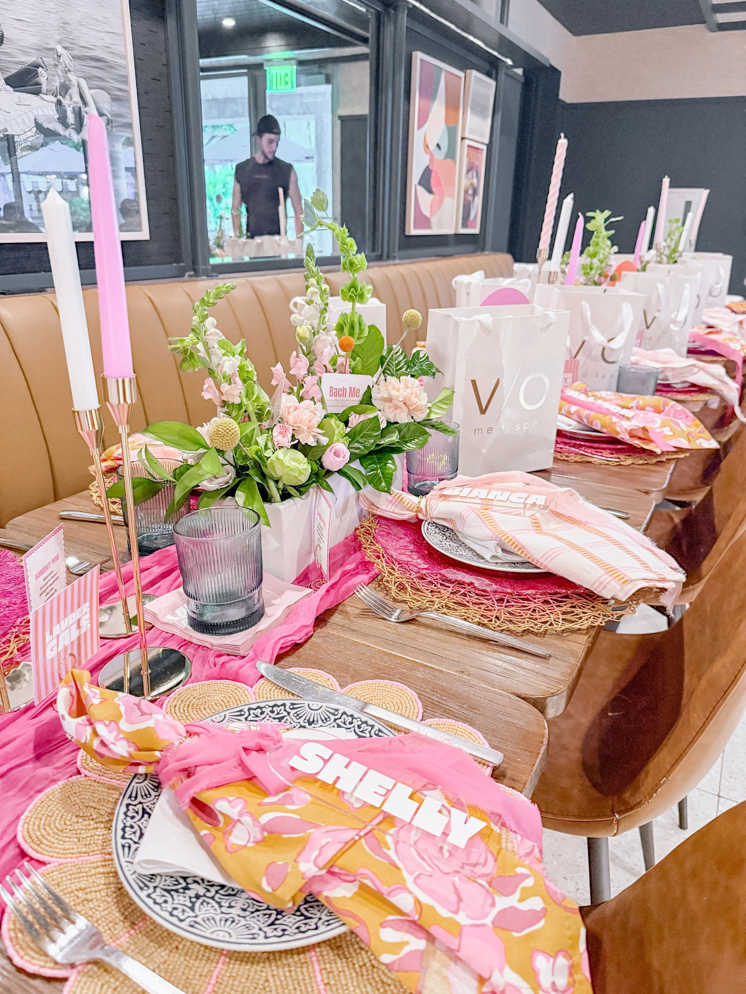 Pink and orange event tablescape with floral centerpieces, candles and styled place settings.