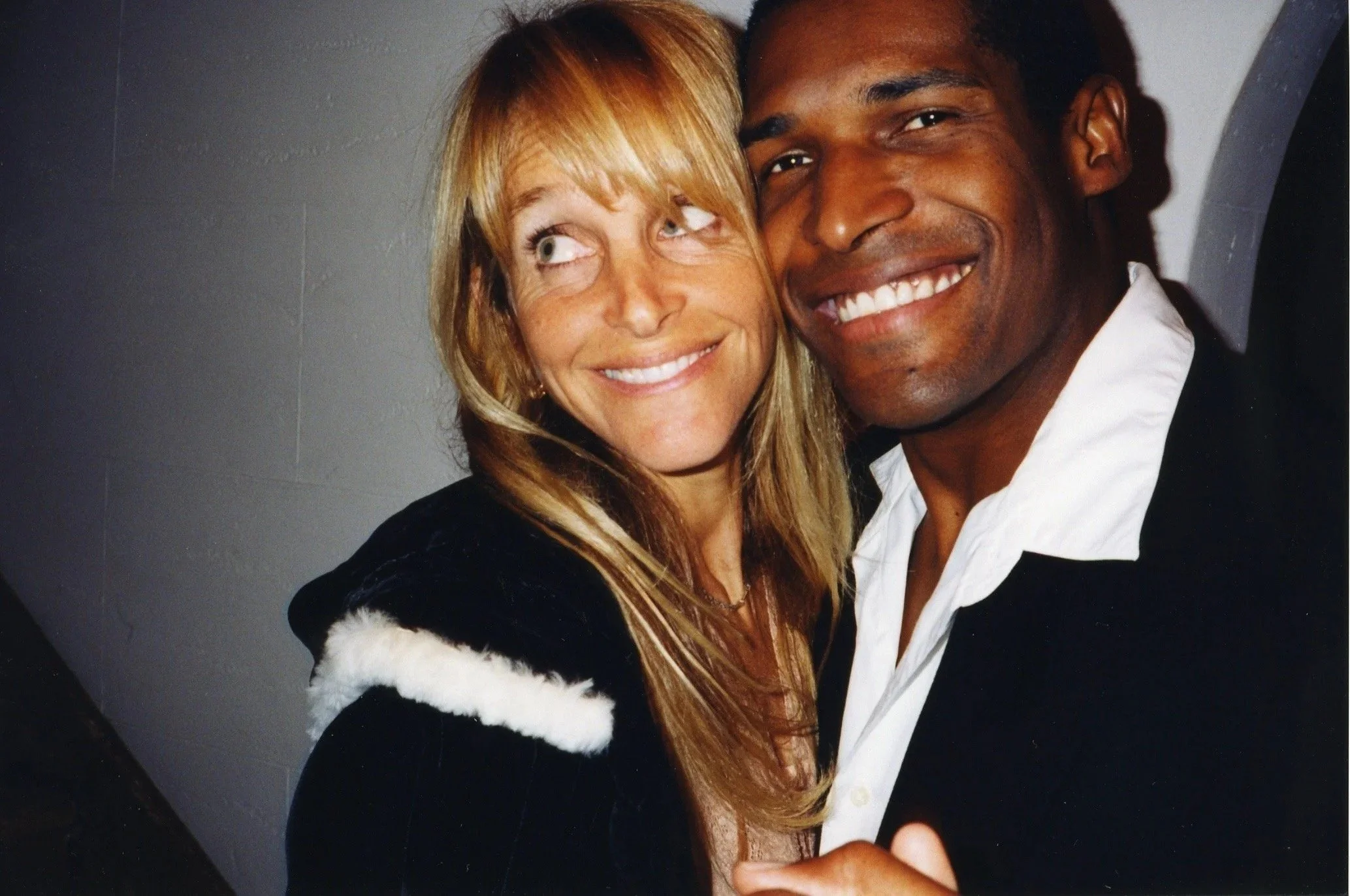 A smiling woman with blonde hair and a man with short dark hair smiling, both posing close together against a plain background.