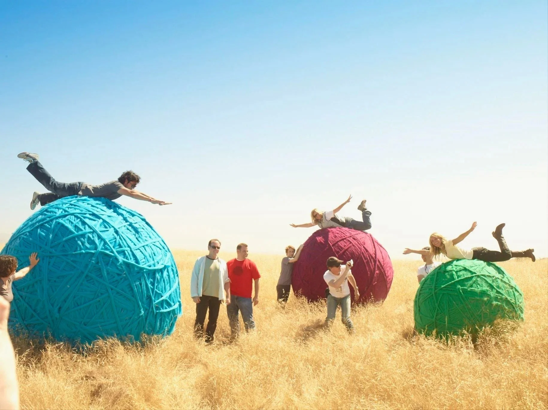People celebrating outdoors with large colorful woven ball sculptures on a sunny day in a field.