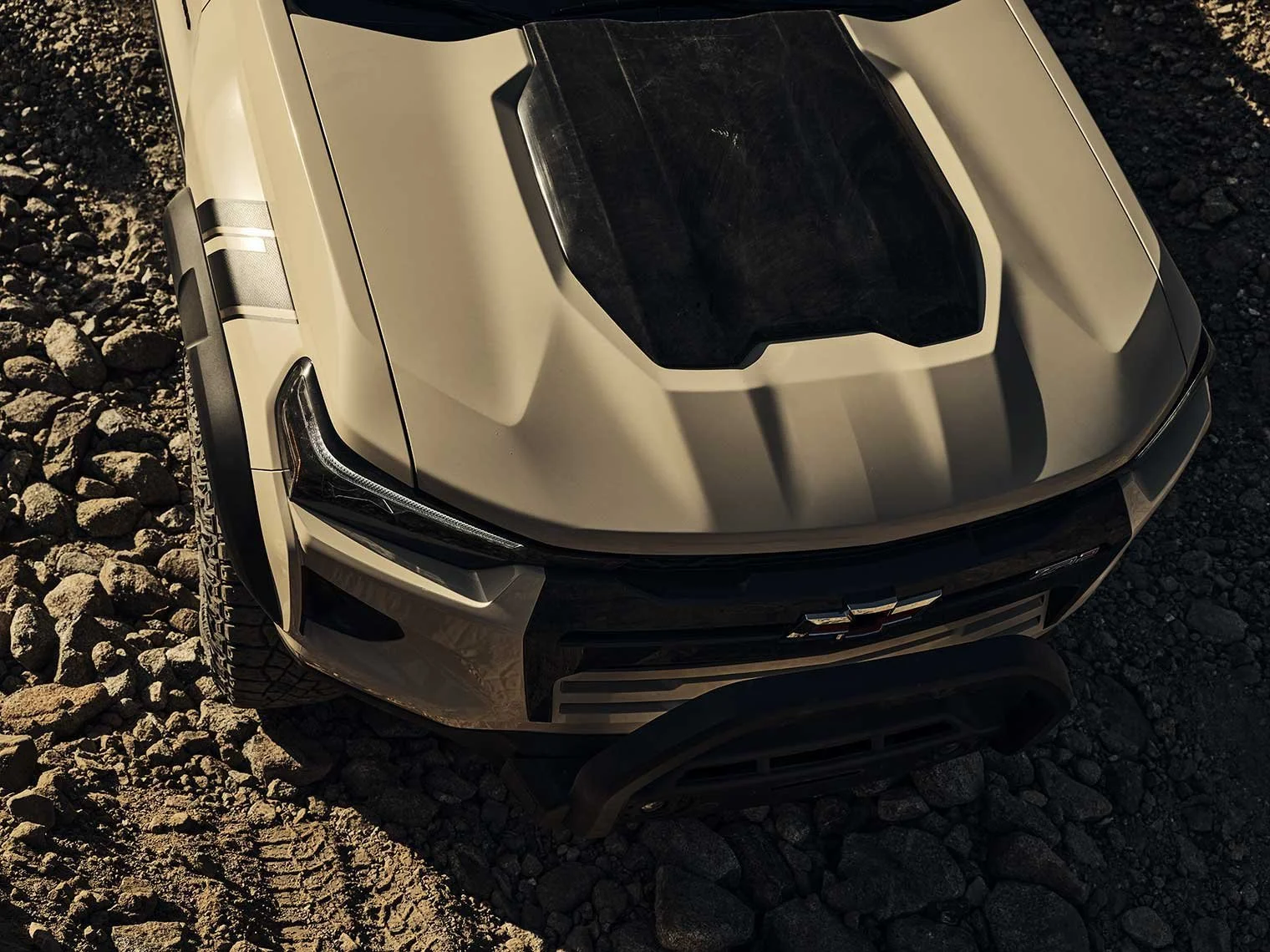Top view of a white off-road sports car with black hood vents parked on rocky terrain.