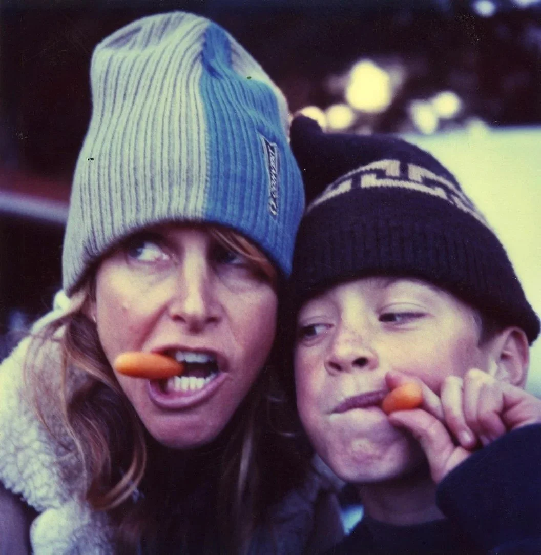 A woman and a boy wearing winter hats sharing a carrot
