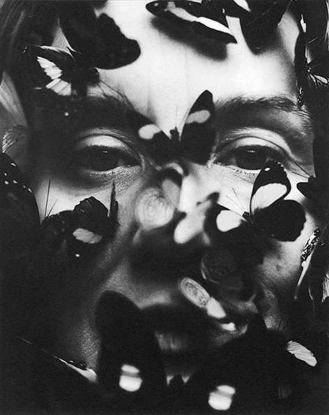 A person's face surrounded by numerous black and white butterflies, some resting on facial features.