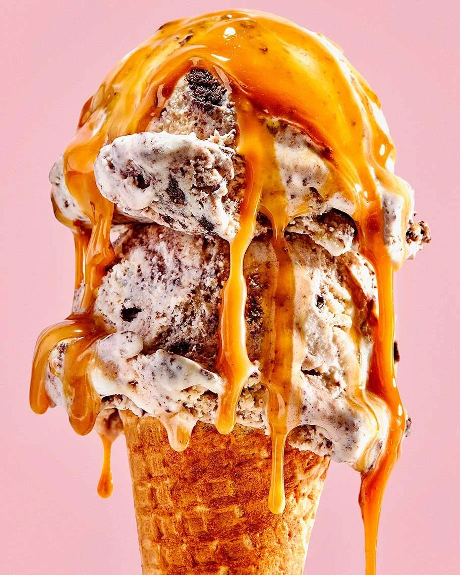 Ice cream cone topped with caramel syrup against a pink background.