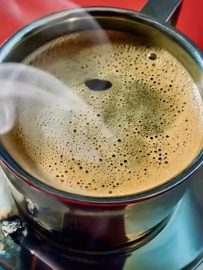 A close-up view of a steaming cup of coffee with frothy foam on top.