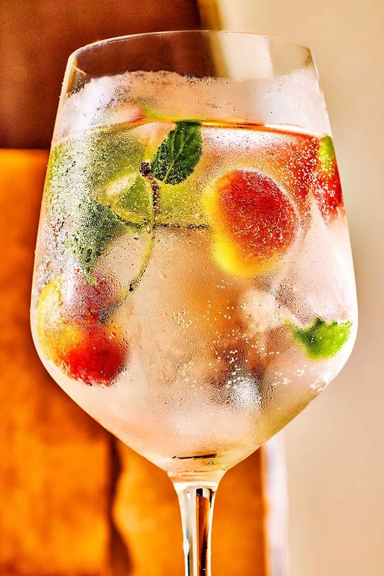 A glass of sparkling water with ice, strawberries, lime, and fresh mint leaves.