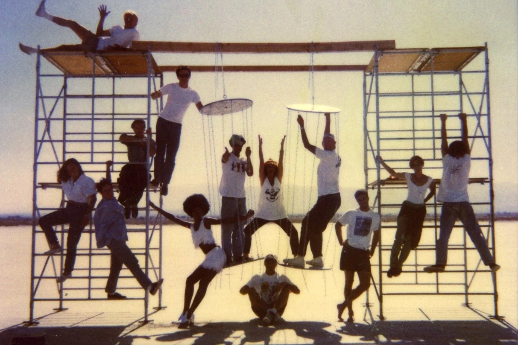 Group of children and teenagers posing on a large metal scaffold structure, with some sitting and others standing, against a clear sky background.