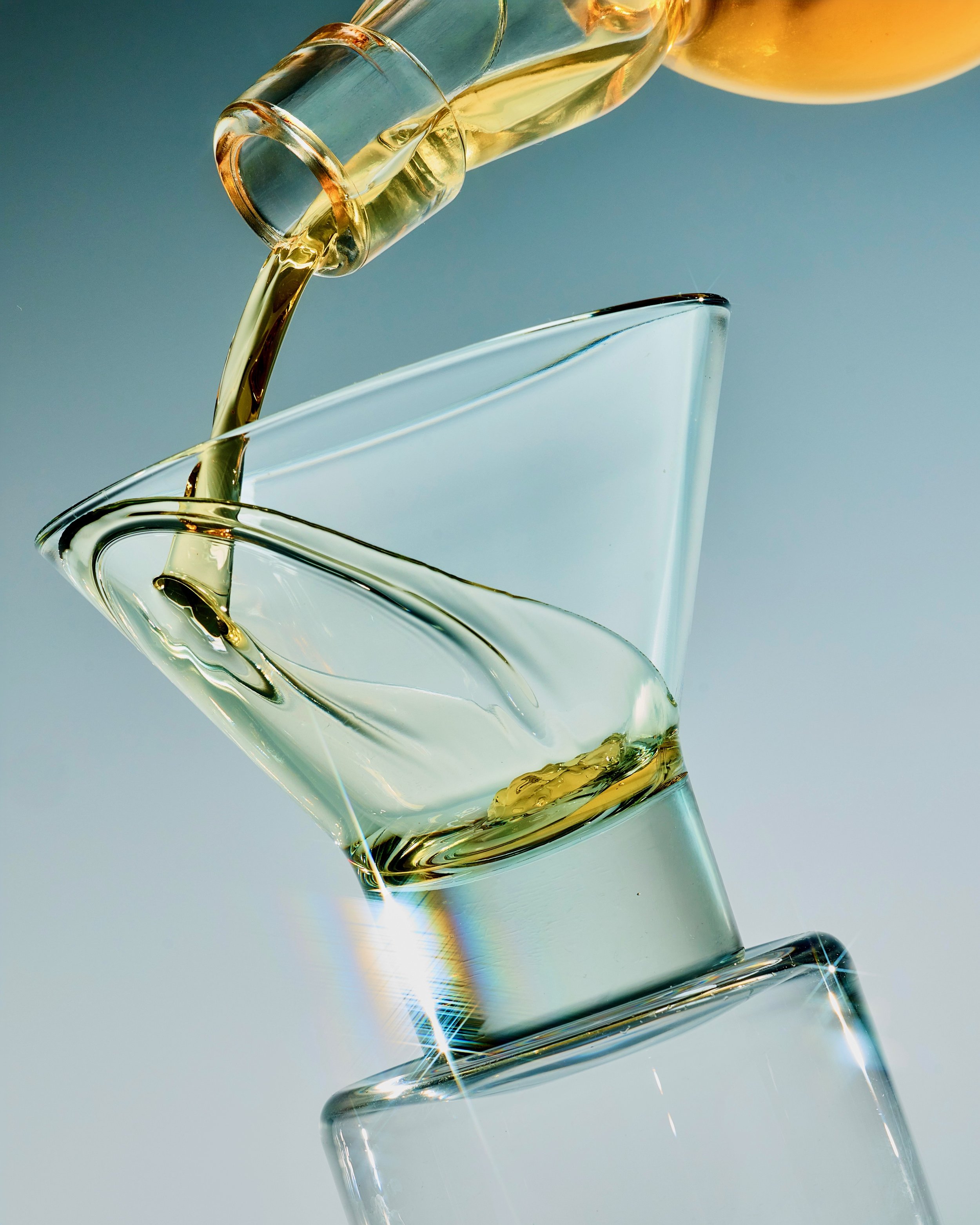 Champagne being poured into a clear glass, with the liquid flowing from a bottle, against a neutral background.
