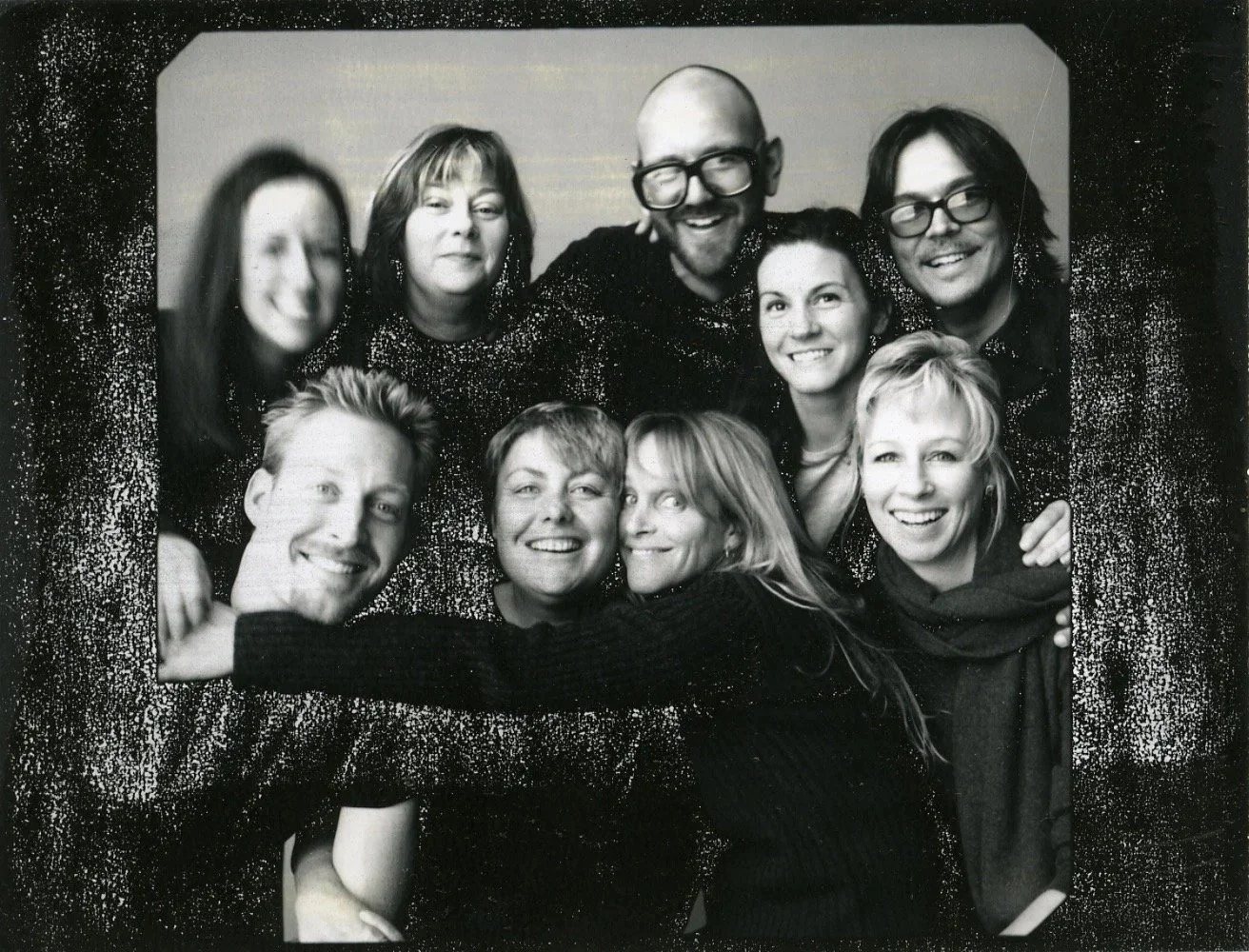 A group of eleven people posing together for a photo with a sparkly background, some smiling, some with more neutral expressions, in black and white.