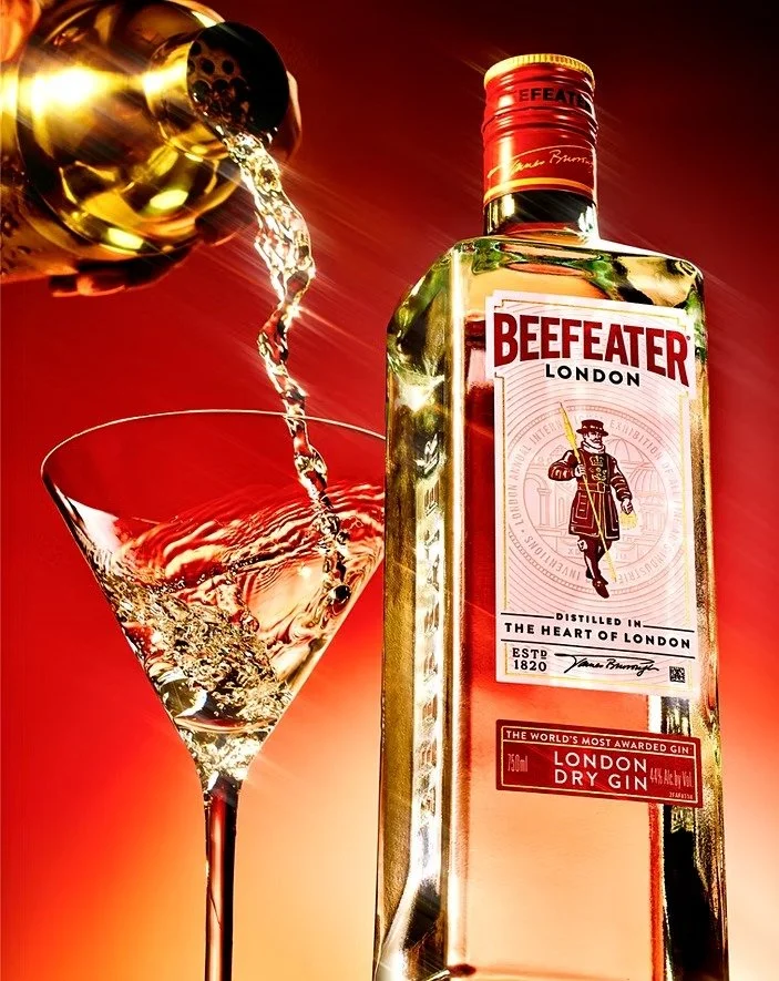A bottle of Beefeater London Dry Gin being poured into a martini glass, with a warm red background.