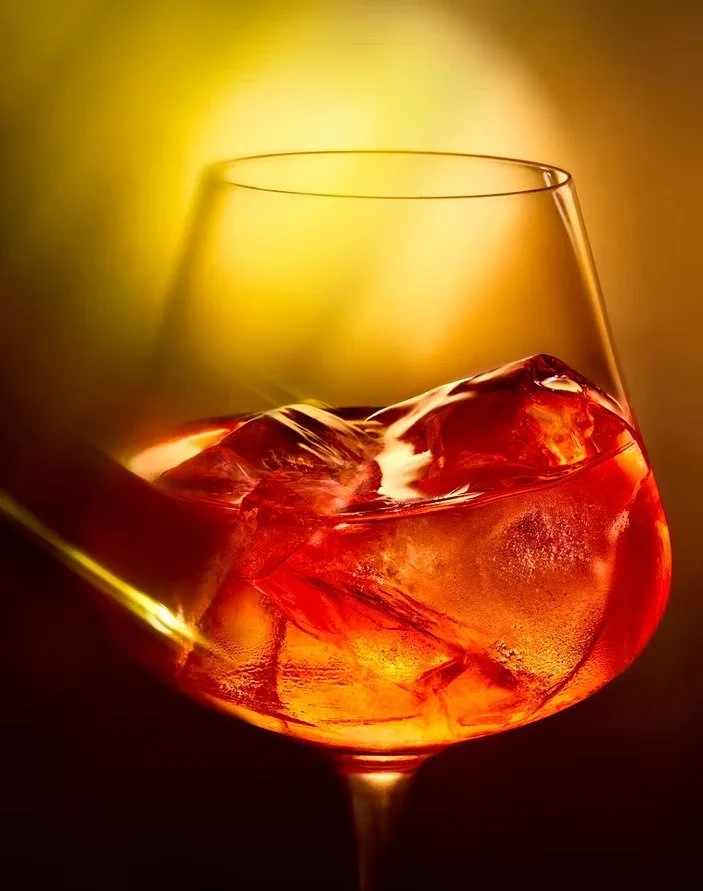 A glass of whiskey with ice cubes, set against a warm golden background.