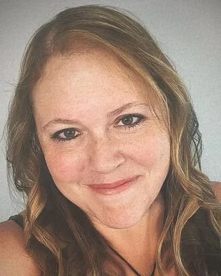 Close-up of a woman with light red hair and freckles, smiling at the camera.