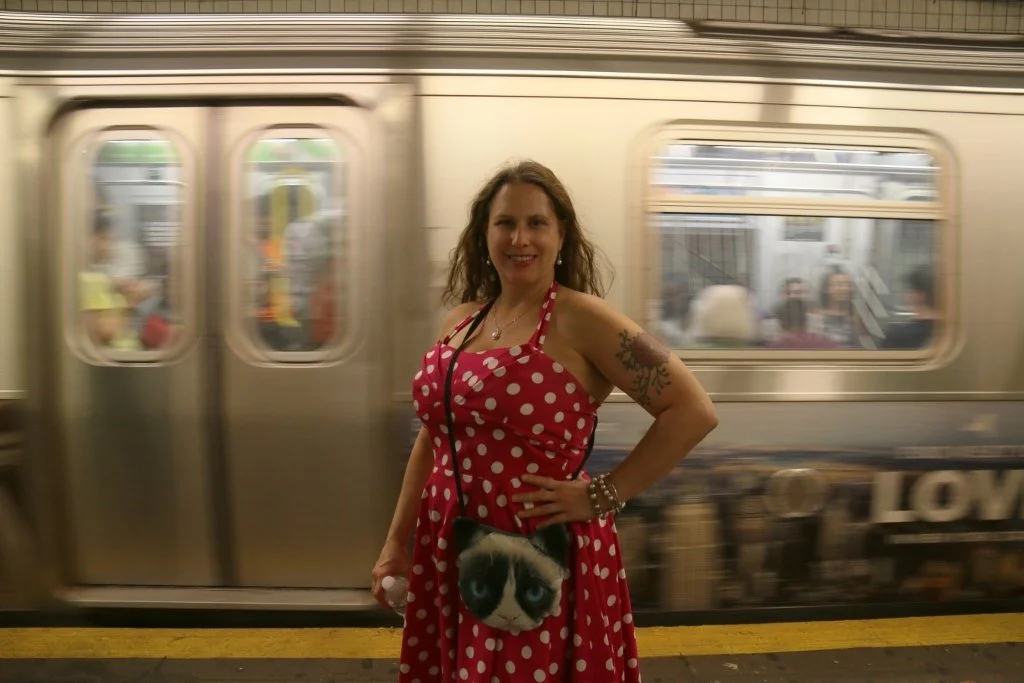 Chintamani stands in front of a moving subway train in a red polka-dot dress
