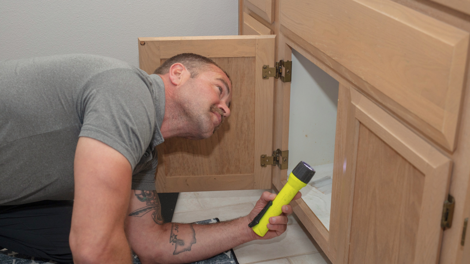 Home inspector checking under-sink plumbing with a flashlight during a home inspection