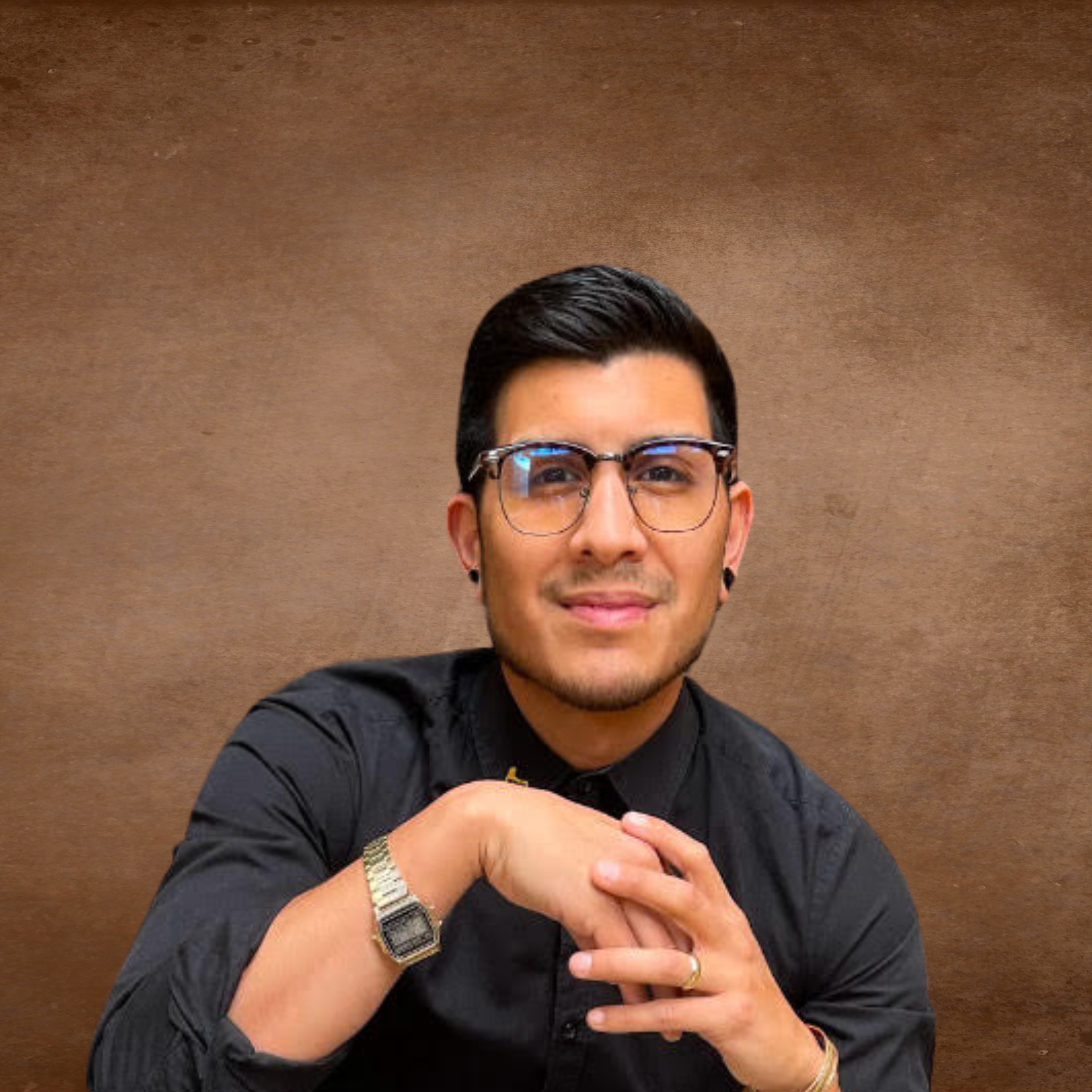 A young man with dark hair and glasses smiling at the camera, hands clasped together, wearing a black shirt, against a brown textured background.