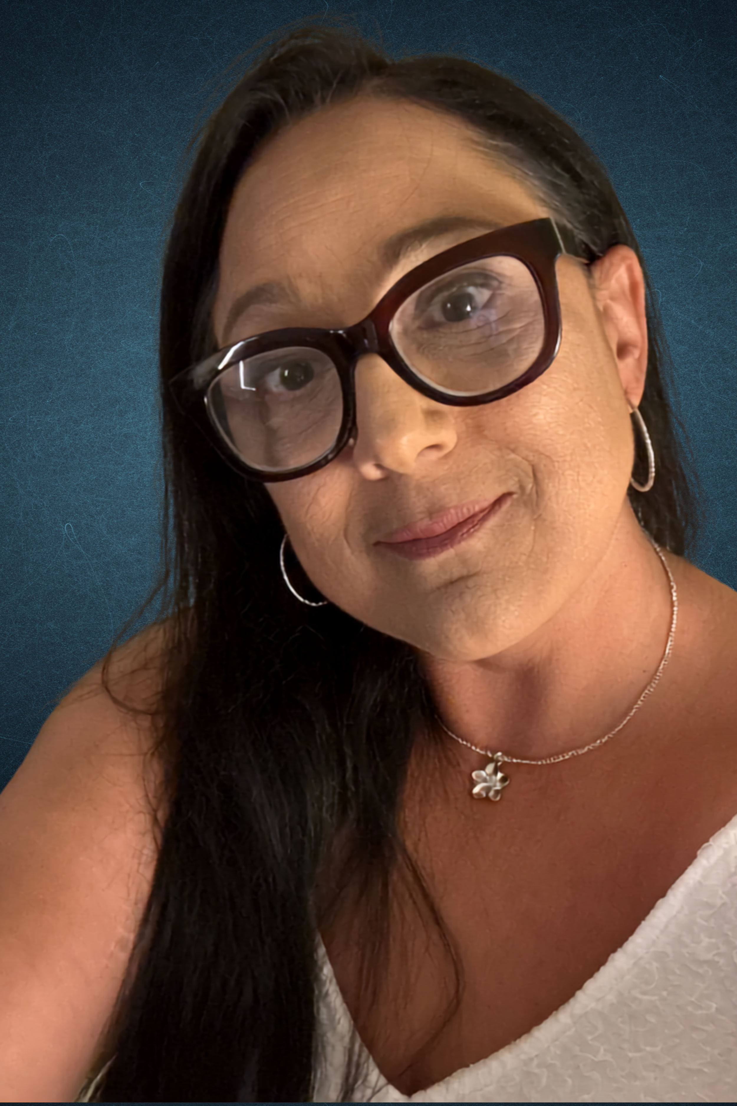 A woman wearing large dark brown glasses, silver hoop earrings, a silver necklace with a flower pendant, and a white bathrobe, with long dark hair and a light skin tone, smiling softly against a dark blue background.