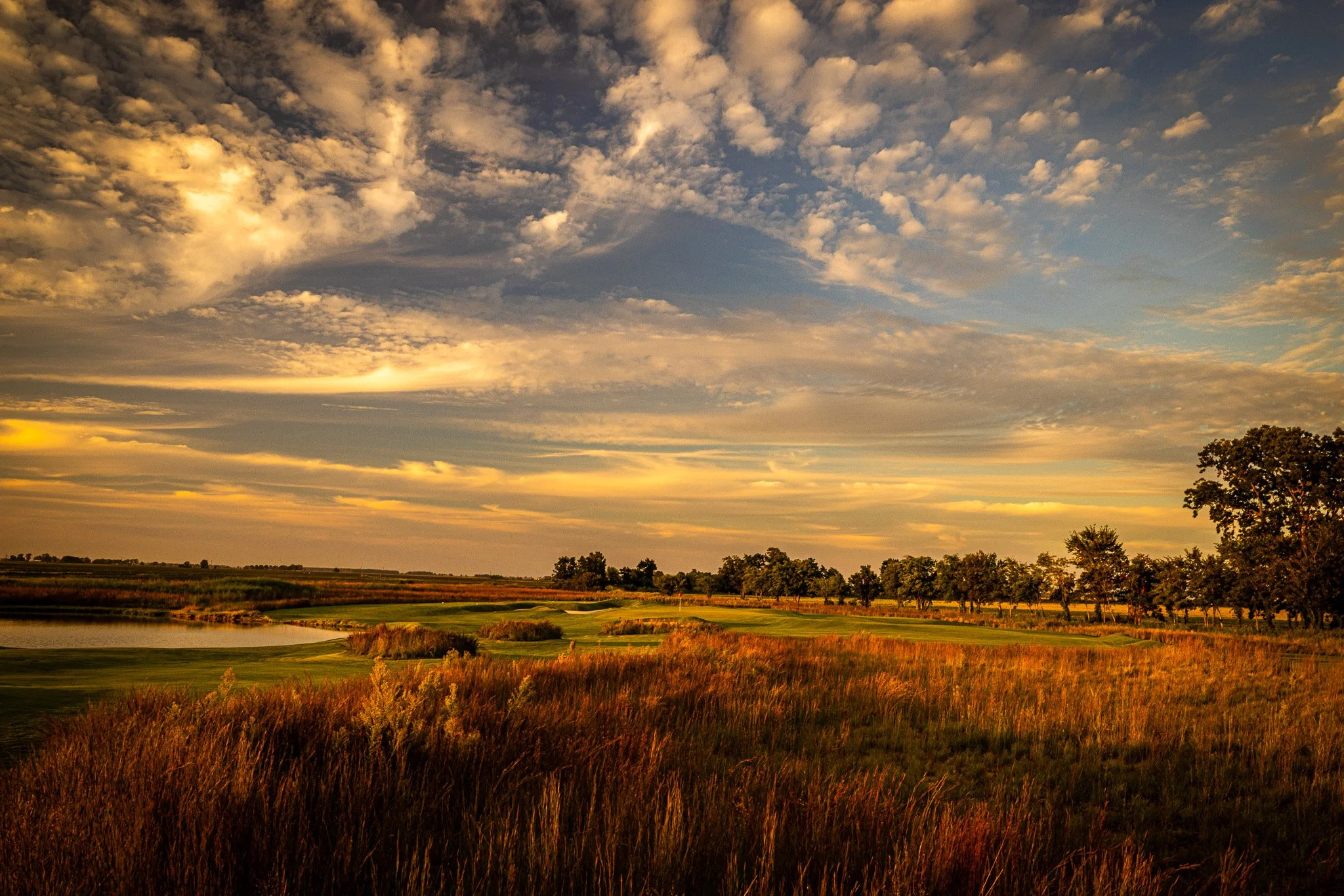 A scenic view of a partly cloudy sky during sunset over a golf course, with trees and water features.