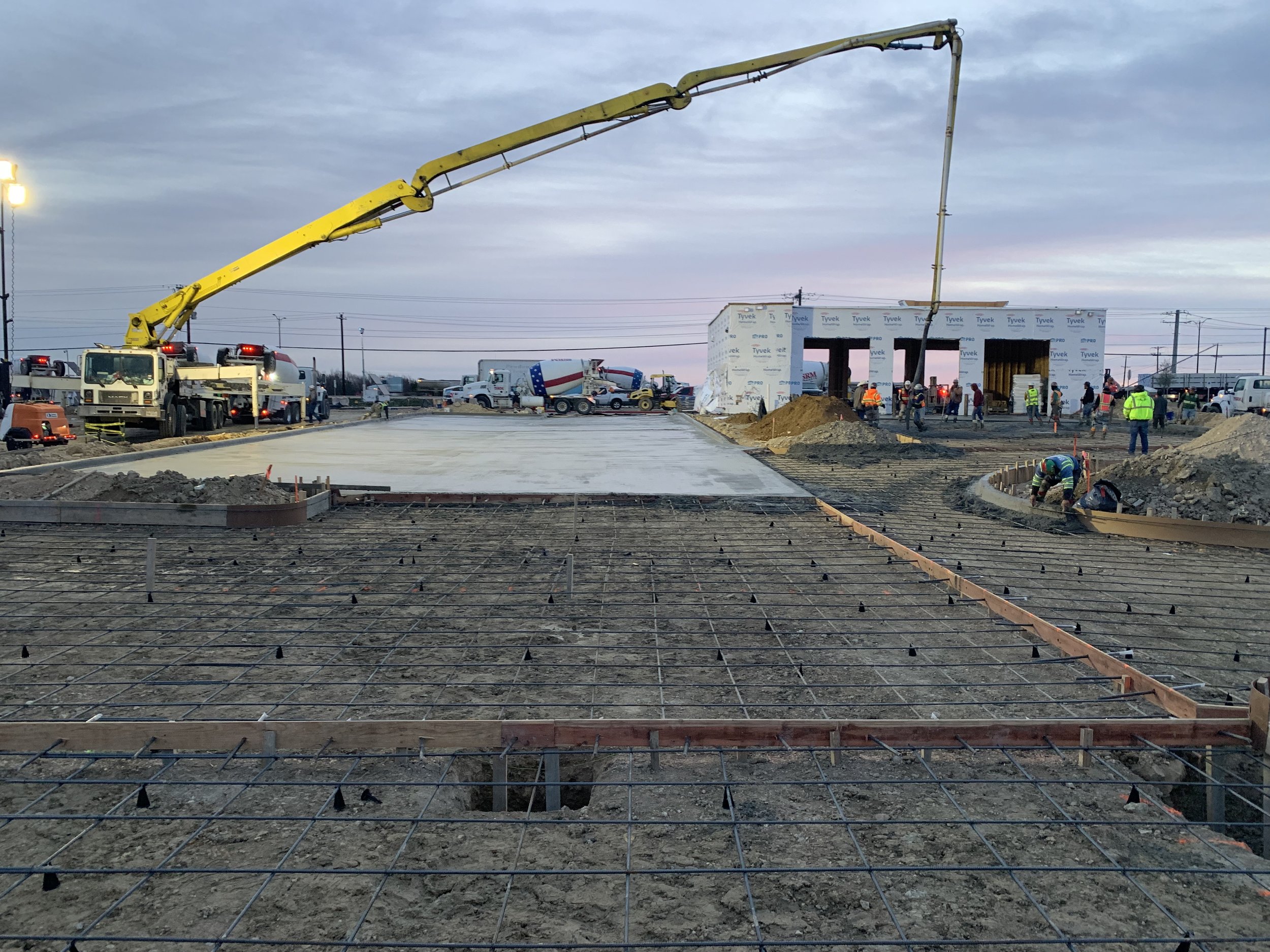 Construction site with workers, concrete pouring truck, and rebar framework for building foundation.