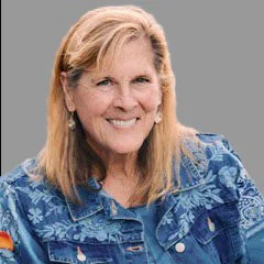 A smiling woman with shoulder-length blonde hair wearing a blue patterned shirt