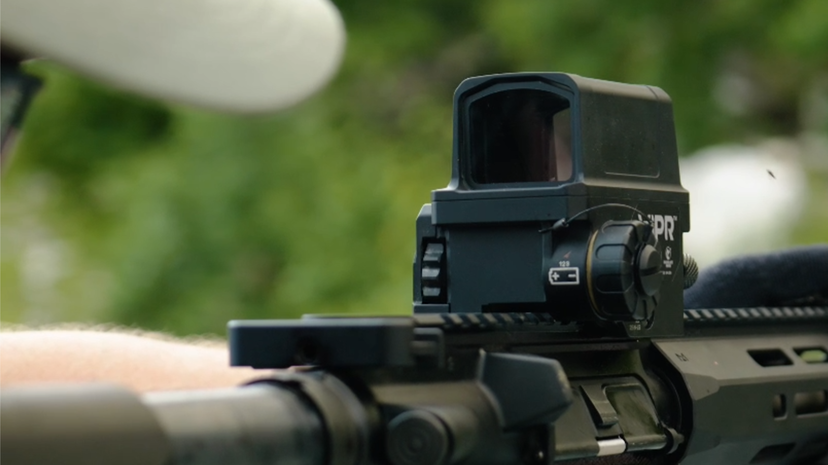Close-up of a firearm's sight with a VIPR Wilcox scope mounted on top, set against a blurred outdoor background.