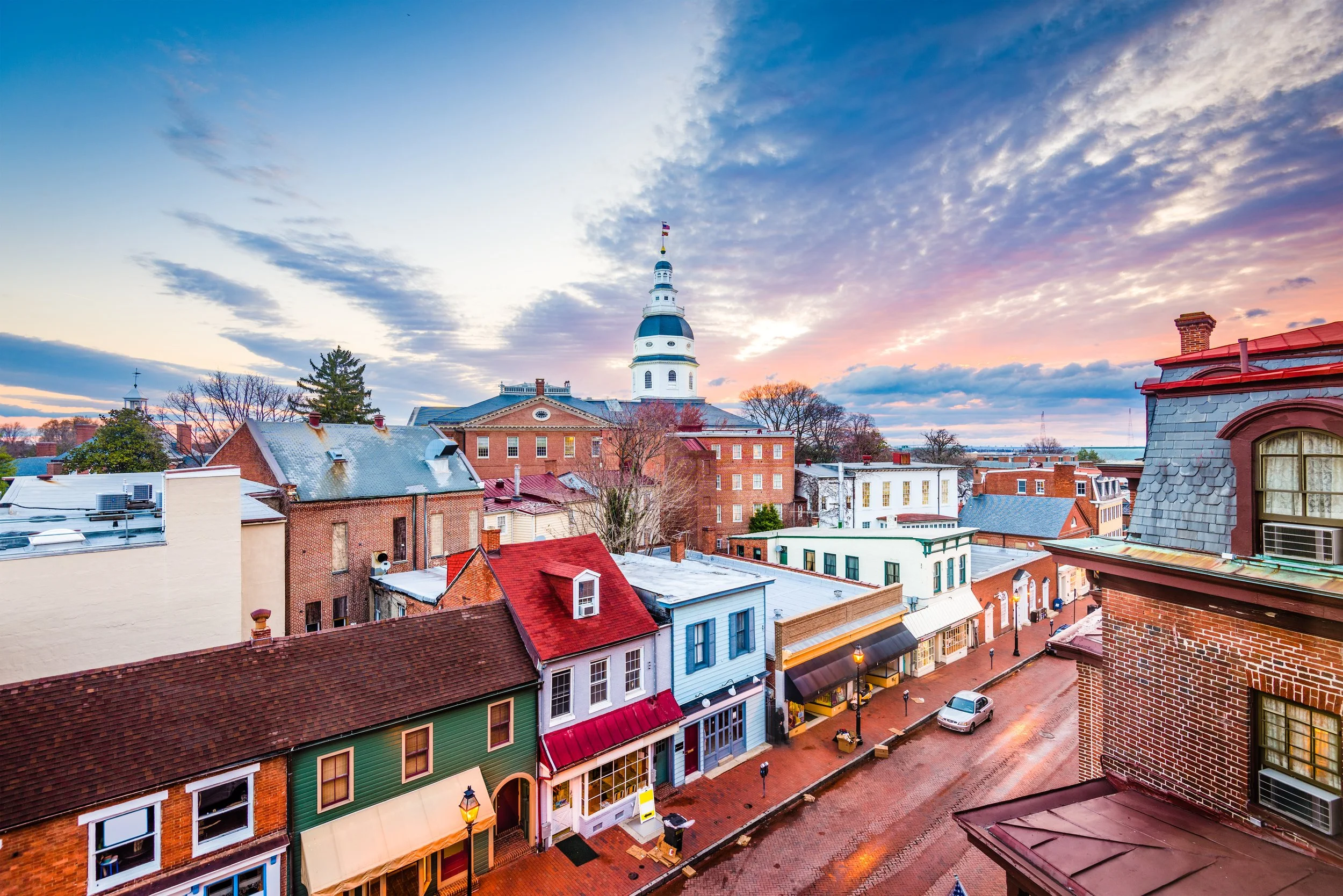 View of a historic town with colorful row houses, a church steeple, and a cloudy sky during sunset.