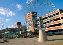 Modern parking garage and cityscape with a Ferris wheel in the background under a blue sky.